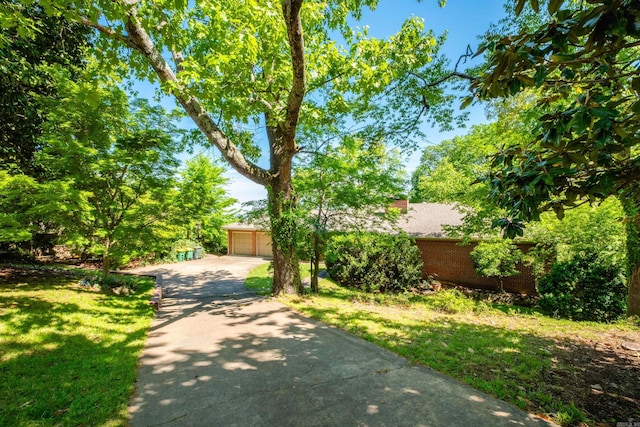 view of front of home featuring a front lawn, a detached garage, driveway, a chimney, and brick siding