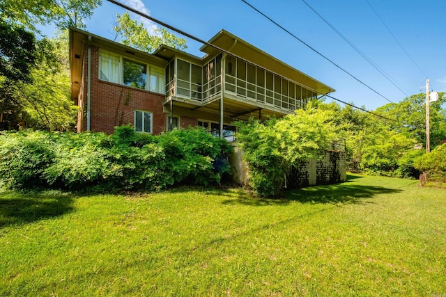 back of house with brick siding, a yard, and a sunroom