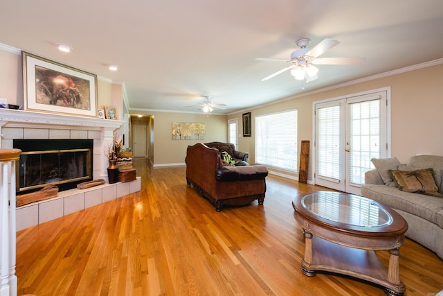 living area with a tile fireplace, wood finished floors, a ceiling fan, ornamental molding, and baseboards