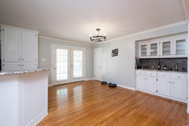 unfurnished dining area featuring light wood-type flooring, ornamental molding, french doors, and an inviting chandelier