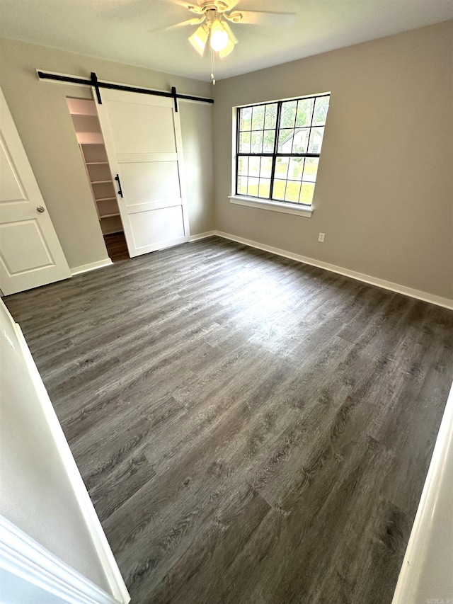 unfurnished bedroom with a barn door, dark wood-style floors, and baseboards