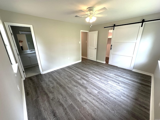 unfurnished bedroom with a barn door, dark wood finished floors, baseboards, and ensuite bathroom