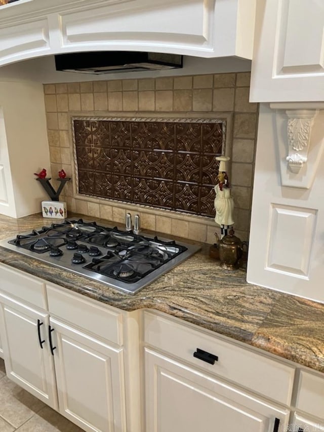 kitchen featuring stainless steel gas stovetop, white cabinetry, decorative backsplash, and dark stone countertops