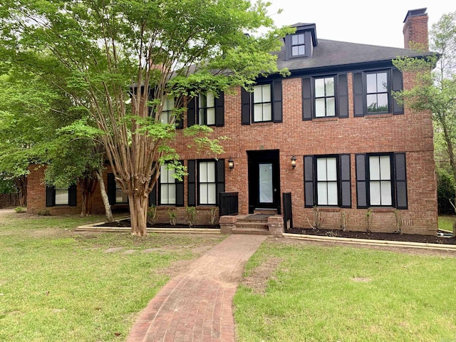 colonial home featuring a front lawn, brick siding, and a chimney