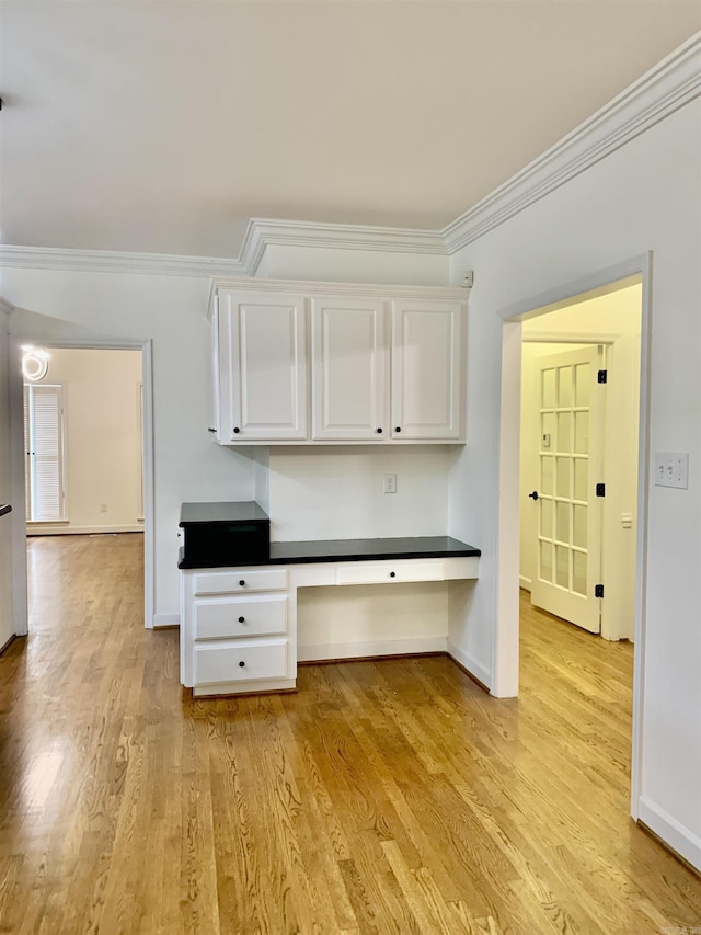 interior space with baseboards, light wood-style flooring, built in desk, and crown molding