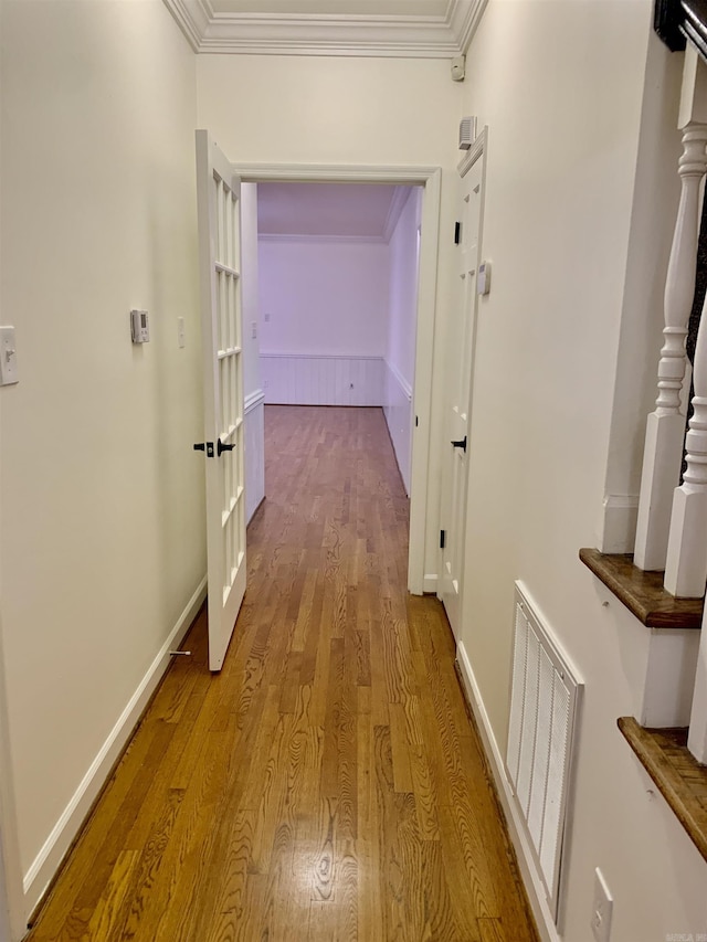 hallway featuring baseboards, crown molding, wood finished floors, and visible vents