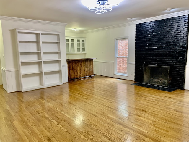 unfurnished living room with crown molding, light wood-type flooring, a wainscoted wall, a fireplace, and a notable chandelier