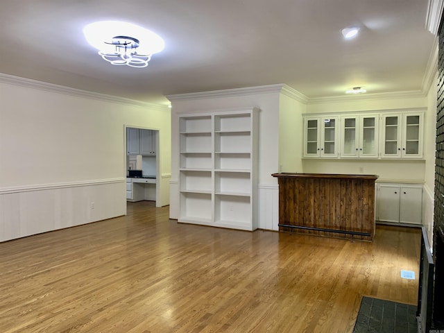 unfurnished living room with wood finished floors, built in features, a notable chandelier, and ornamental molding
