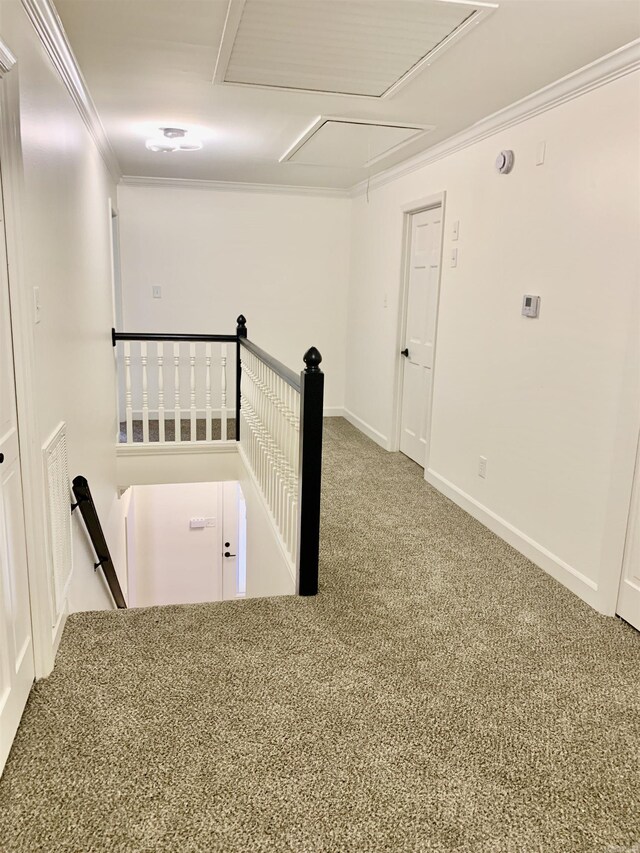 carpeted empty room with attic access, baseboards, and ornamental molding