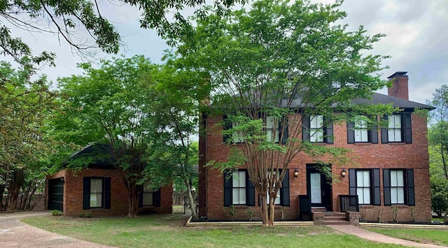 colonial inspired home with brick siding, a chimney, a front yard, and a garage