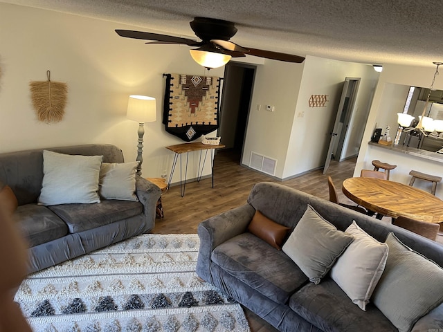 living area featuring a textured ceiling, baseboards, visible vents, wood finished floors, and ceiling fan