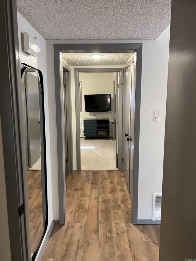 hall featuring wood finished floors, a textured ceiling, and visible vents