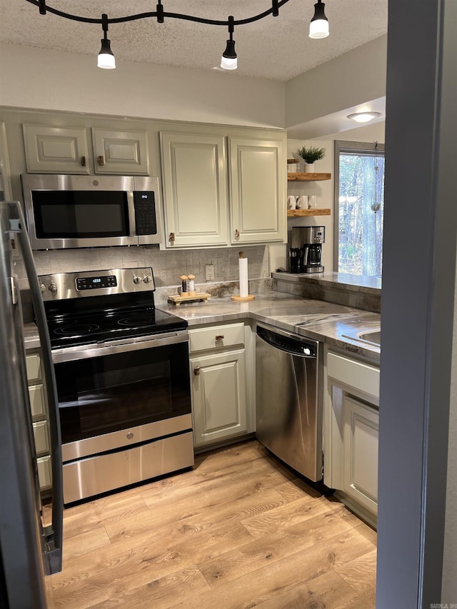 kitchen with a textured ceiling, backsplash, light wood-style floors, open shelves, and appliances with stainless steel finishes