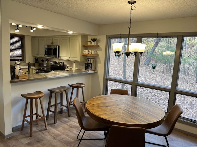dining space featuring track lighting, light wood-style flooring, a textured ceiling, and an inviting chandelier