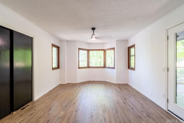unfurnished room with ornamental molding, wood finished floors, a textured ceiling, and plenty of natural light