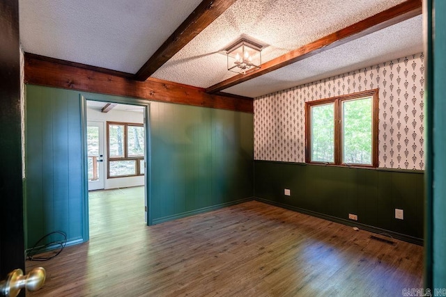 unfurnished room with beamed ceiling, wood finished floors, visible vents, and a textured ceiling