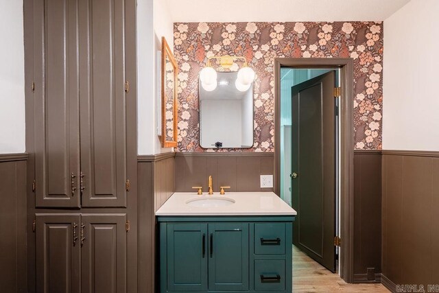 bathroom with wainscoting, vanity, wood finished floors, and wallpapered walls