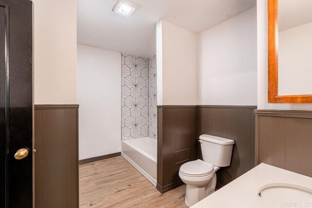 bathroom featuring wood finished floors, toilet, a wainscoted wall, and a sink
