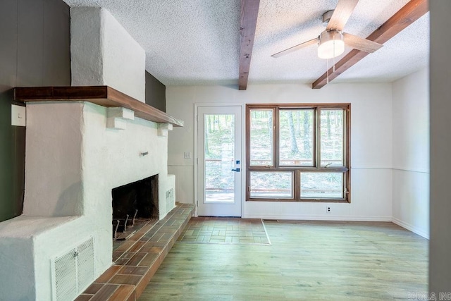 unfurnished living room with a textured ceiling, light wood-type flooring, beamed ceiling, a fireplace, and visible vents