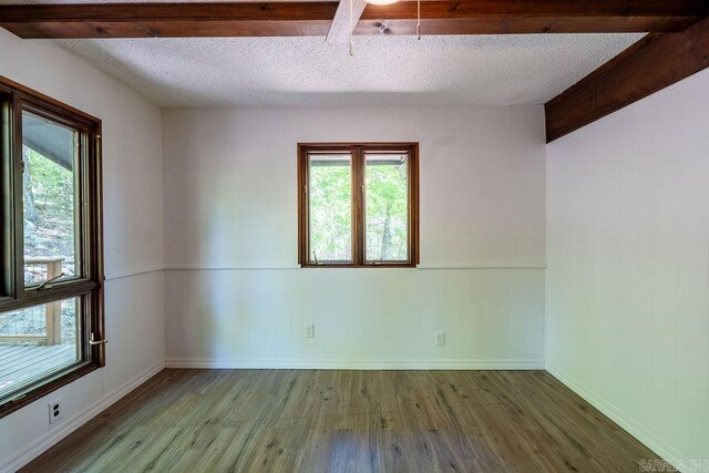 unfurnished room with wood finished floors, a textured ceiling, plenty of natural light, and wainscoting