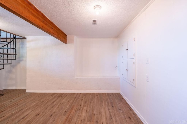 empty room with wood finished floors, a textured ceiling, baseboards, beam ceiling, and visible vents