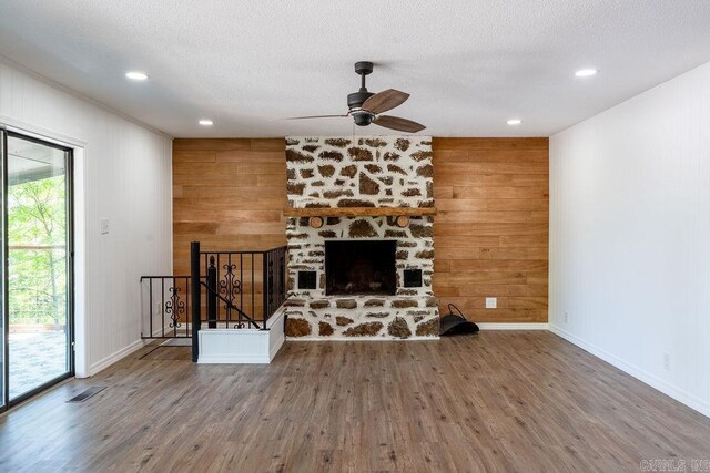 unfurnished living room featuring a stone fireplace, wood finished floors, ceiling fan, baseboards, and visible vents