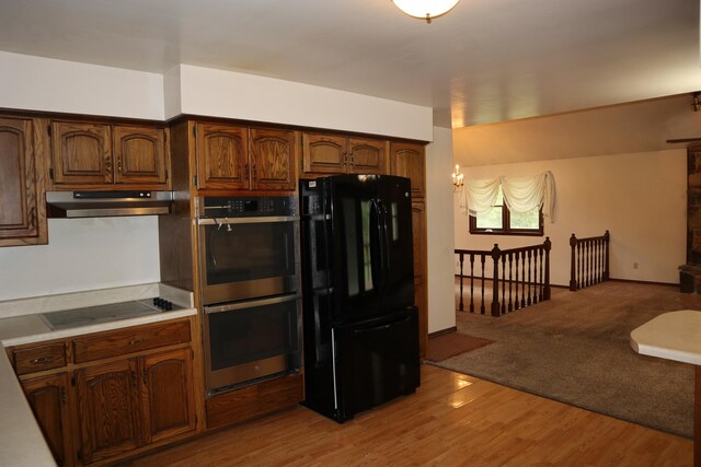 kitchen with black appliances, open floor plan, light wood finished floors, light countertops, and under cabinet range hood