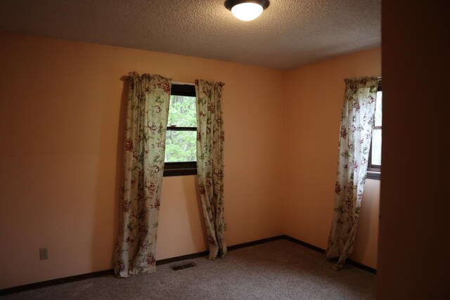 carpeted empty room with baseboards, a textured ceiling, and visible vents