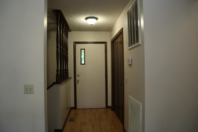 corridor with wood finished floors, visible vents, and a textured ceiling