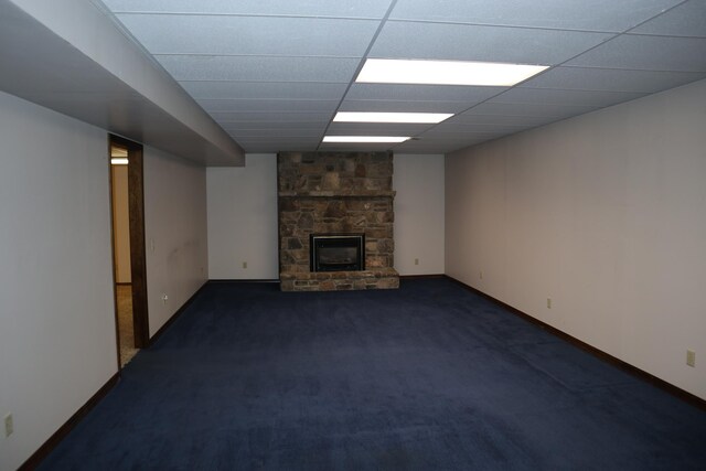 unfurnished living room with dark carpet, a stone fireplace, and baseboards