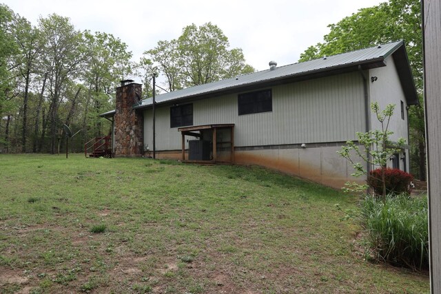 back of house with cooling unit, a yard, a chimney, and metal roof