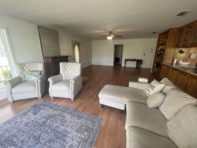 living area featuring a fireplace, wood finished floors, visible vents, and a ceiling fan