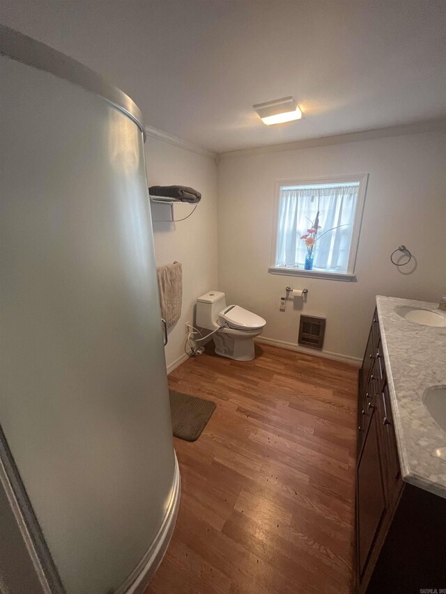 bathroom featuring toilet, baseboards, heating unit, wood finished floors, and vanity