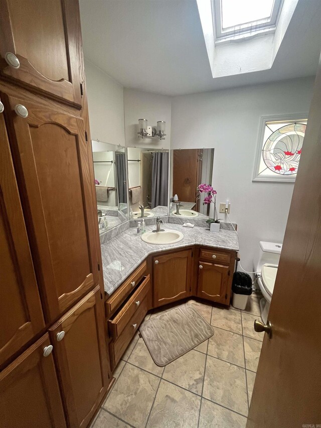 bathroom with tile patterned floors, a skylight, vanity, and toilet