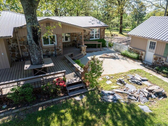 rear view of property with a standing seam roof, stone siding, fence, metal roof, and a deck