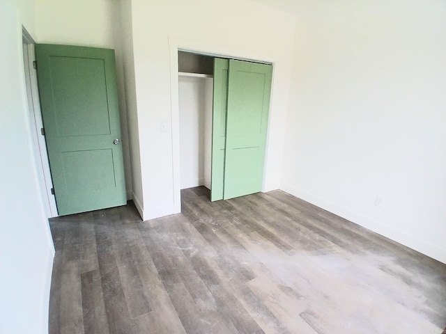 unfurnished bedroom with wood finished floors, baseboards, and a closet