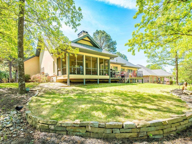back of property featuring a chimney, a yard, stucco siding, a sunroom, and a deck