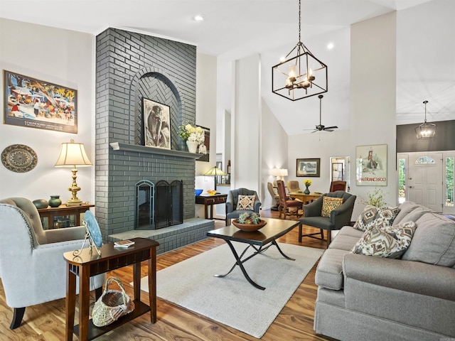 living area with a chandelier, recessed lighting, a towering ceiling, wood finished floors, and a fireplace