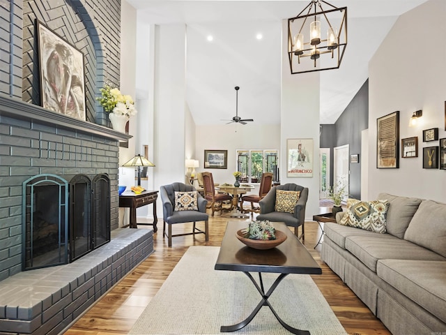 living area with ceiling fan with notable chandelier, a brick fireplace, wood finished floors, and high vaulted ceiling