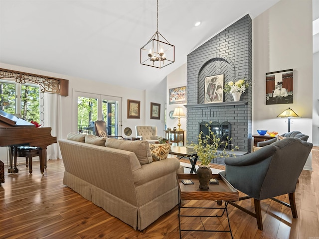 living area with wood finished floors, a brick fireplace, high vaulted ceiling, and a notable chandelier