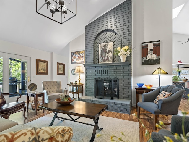 living room featuring wood finished floors, a brick fireplace, high vaulted ceiling, and a notable chandelier