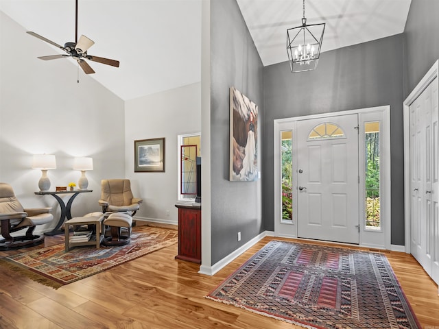 foyer featuring high vaulted ceiling, baseboards, wood finished floors, and ceiling fan with notable chandelier