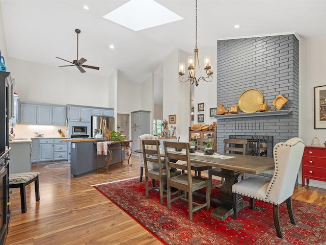 dining space featuring light wood finished floors, a skylight, high vaulted ceiling, and ceiling fan with notable chandelier