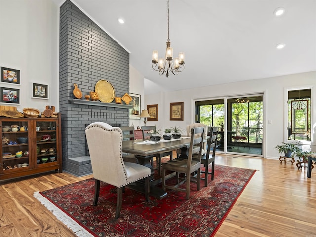 dining space featuring a brick fireplace, wood finished floors, high vaulted ceiling, and a notable chandelier