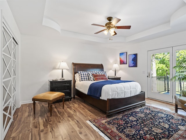 bedroom featuring a tray ceiling, wood finished floors, ceiling fan, and access to outside
