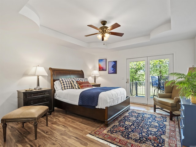 bedroom featuring a ceiling fan, access to outside, light wood-style flooring, and a raised ceiling