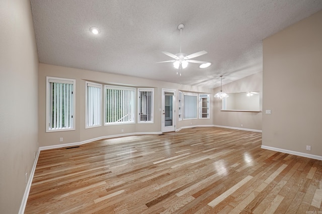 unfurnished living room with lofted ceiling, light wood finished floors, baseboards, a textured ceiling, and ceiling fan with notable chandelier