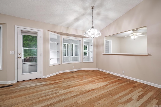 unfurnished dining area with wood finished floors, visible vents, baseboards, a textured ceiling, and a notable chandelier
