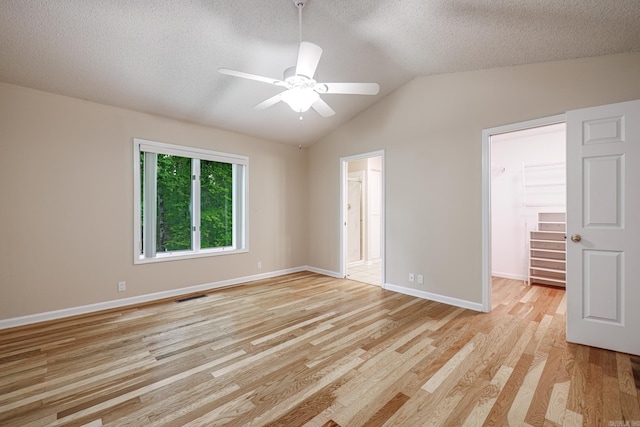 empty room featuring a ceiling fan, a textured ceiling, light wood-style floors, lofted ceiling, and visible vents