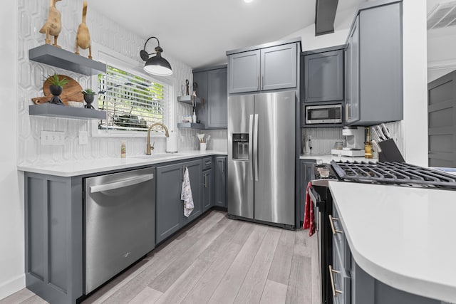 kitchen with open shelves, gray cabinets, stainless steel appliances, and a sink